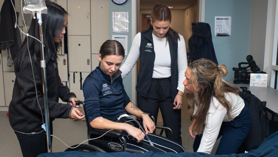 三个物理治疗的学生练习帮助一个坐在轮椅上的病人