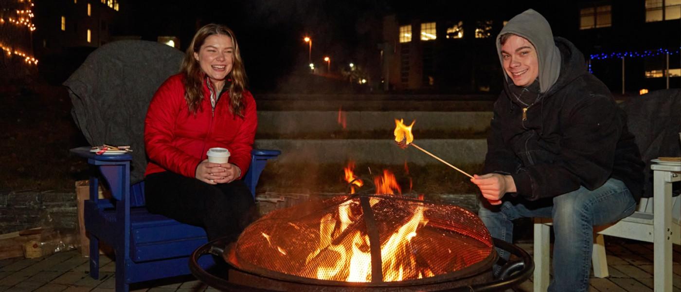 学生 roast marshmallows 和 drink hot cocoa by a bonfire