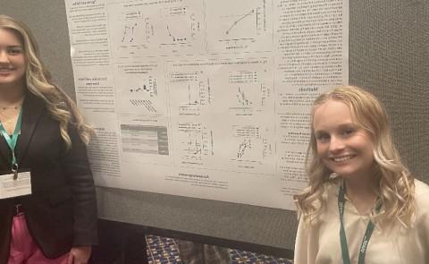 Lily Bennett, ’25 (left), 和汉娜·拉科斯, ’23(右)在杜克大学举行的2023年USASP会议上，在他们的海报前.